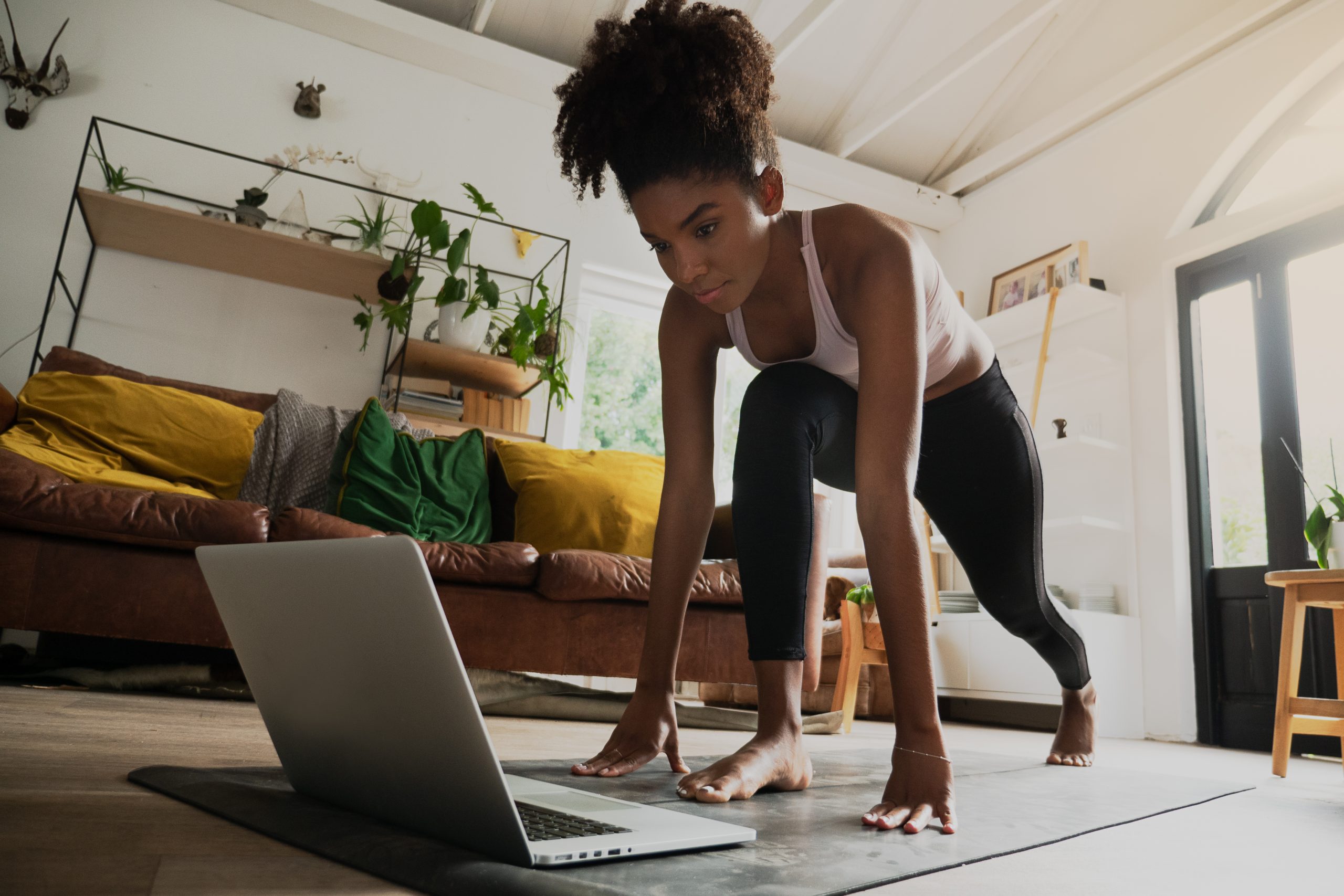Mujer joven haciendo yoga en su sala de estar, mientras mira su ordenador portátil