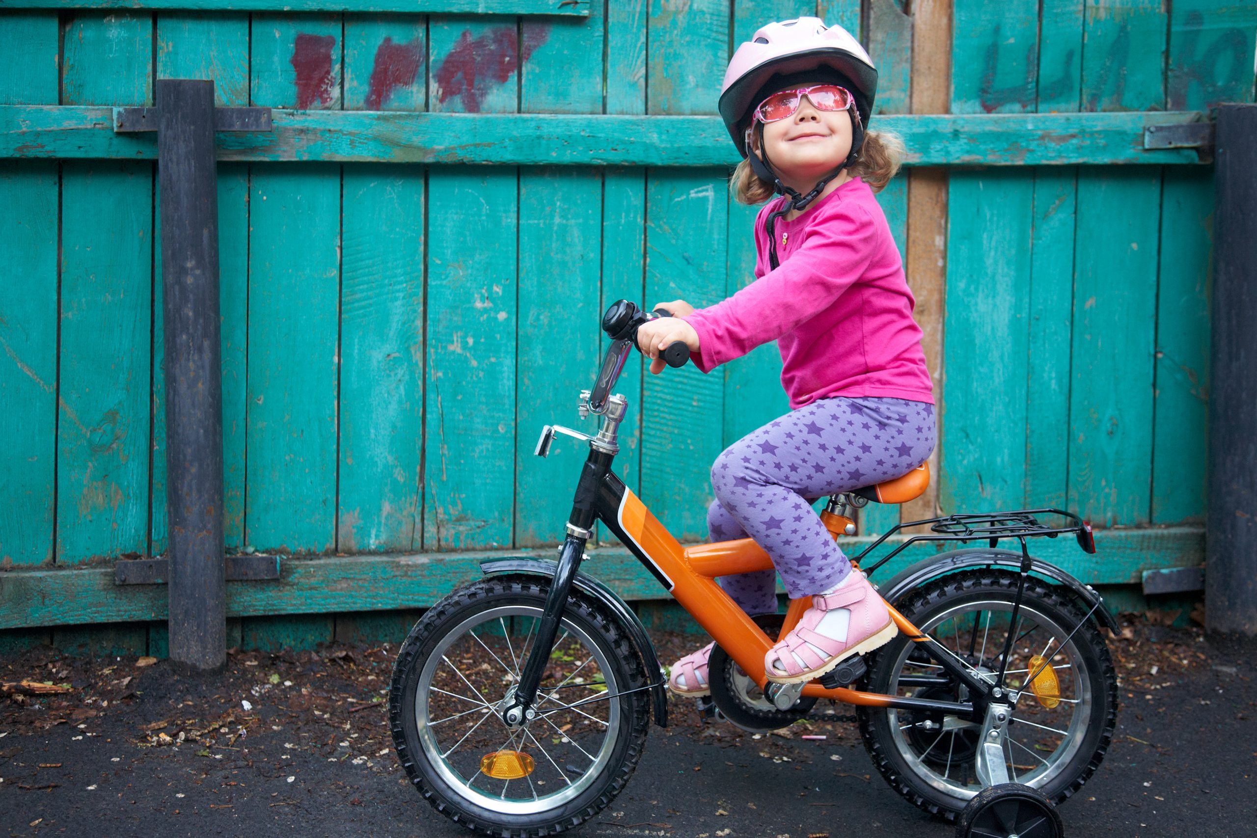 A young girl wearing pink sunglasses and a helmet, riding her bike
