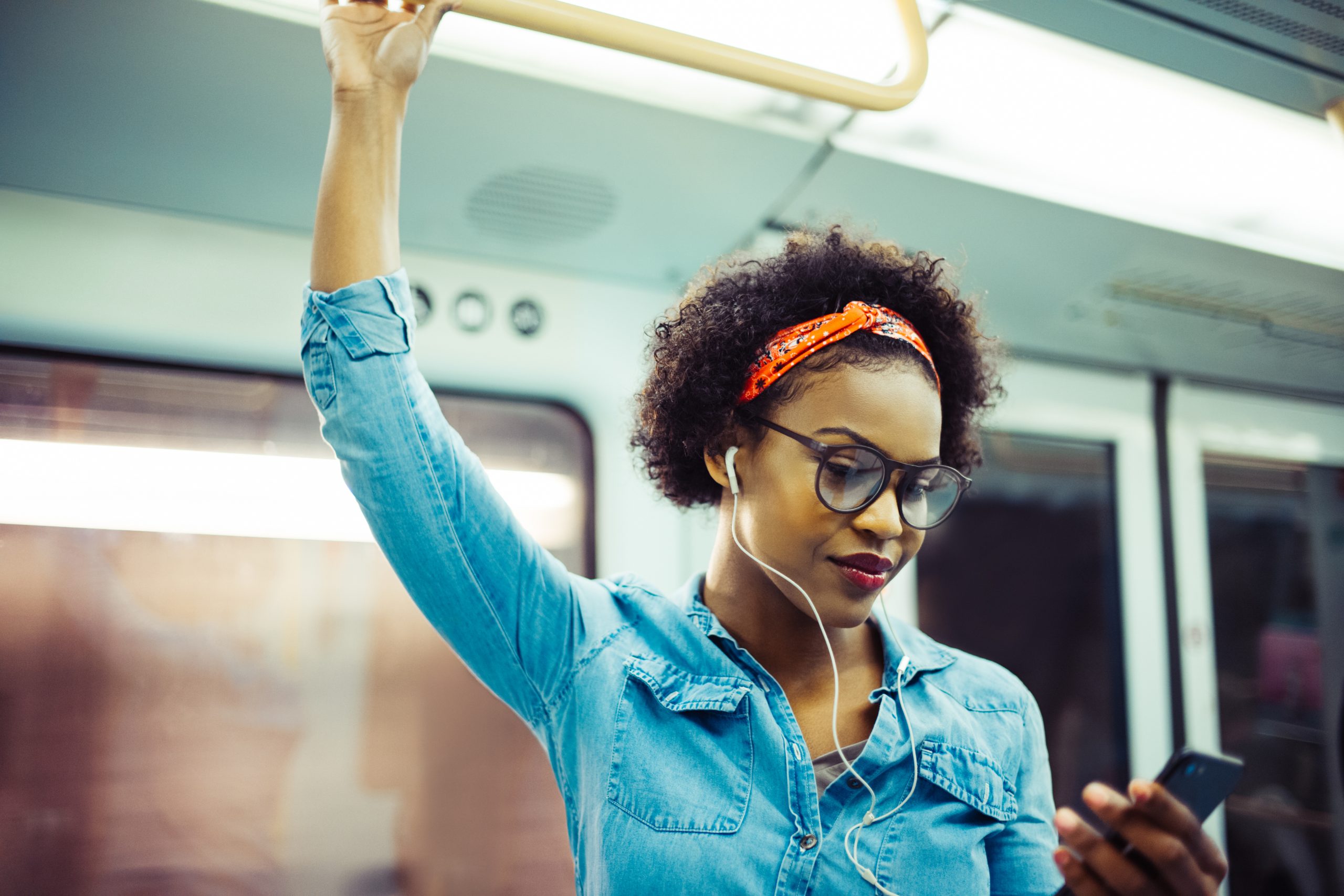 A young woman with headphones, listening to music on her phone on the train