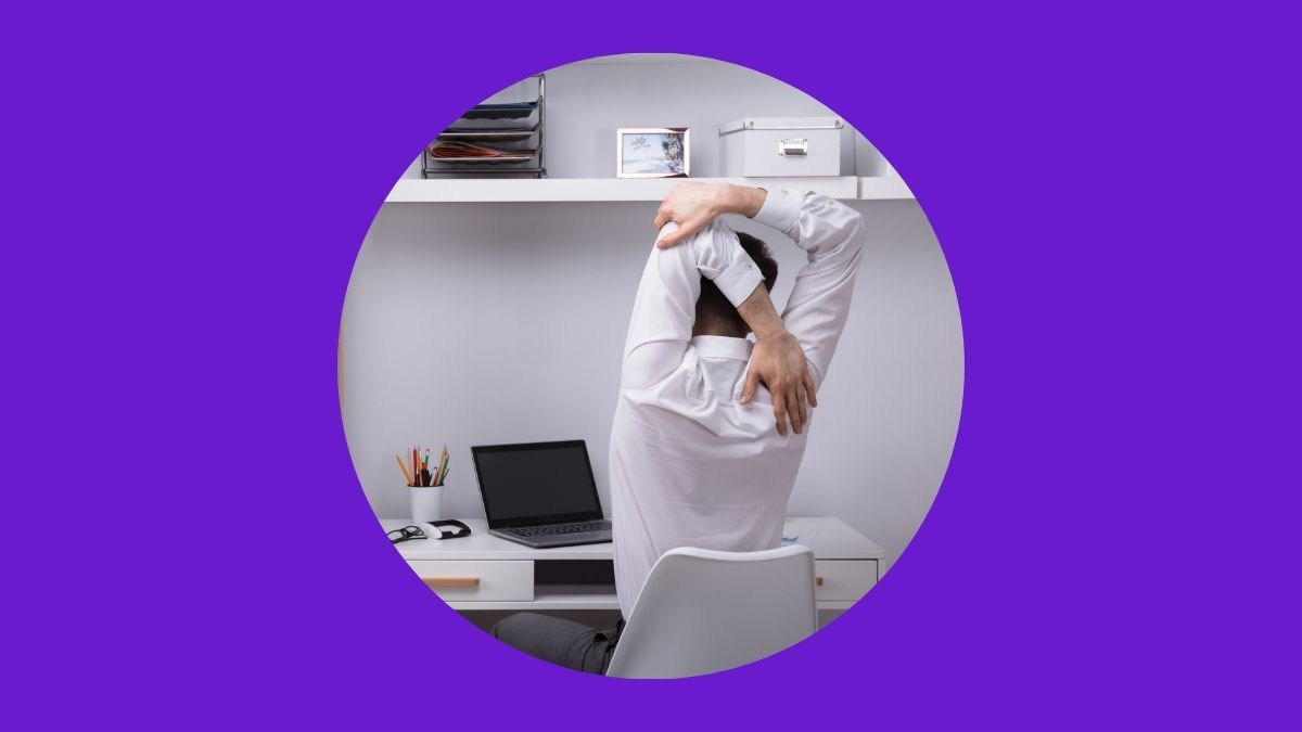 A man in a white shirt, stretching his shoulders at his desk