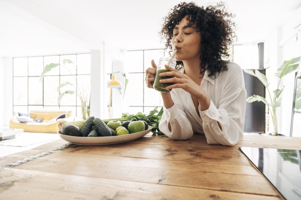 Woman drinking green juice while sitting at table
