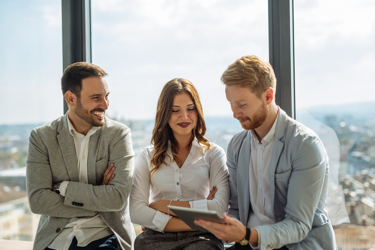 2 men and 1 women standing together while viewing an iPad